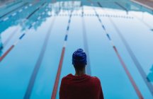 Vista trasera de una joven nadadora envuelta en una toalla cerca de la piscina - foto de stock