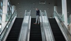 Vista baja del hombre de negocios hablando en el teléfono móvil en la escalera mecánica en la oficina - foto de stock
