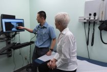 Vista lateral del joven médico asiático discutiendo sobre el informe de rayos X en la computadora en la clínica - foto de stock
