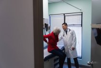 Jeune asiatique mâle médecin vérifier l'os du dos de la femme de la patiente âgée en clinique — Photo de stock