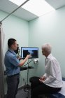 Vista laterale del giovane medico maschio asiatico che discute sopra il rapporto dei raggi X sul computer alla clinica — Foto stock