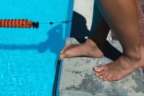 Вид на низьку секцію молодої жінки-плавця, що стоїть на стартовому блоці біля басейну на сонці — стокове фото