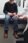 Vue de face du jeune médecin asiatique qui examine le genou d'un garçon caucasien dans une clinique. Médecin masculin utilisant le marteau réflexe — Photo de stock