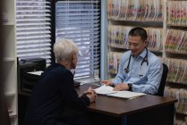 Joven asiático médico y paciente senior interactuando entre sí en la clínica - foto de stock