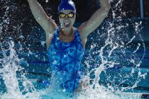 Vista frontal de una joven nadadora divirtiéndose y levantando las manos en la piscina - foto de stock