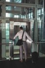 Rear view of businessman with travel bag calling for the elevator in office — Stock Photo