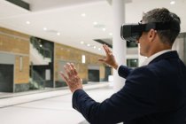 Вид збоку бізнесмена, який відчуває гарнітуру VR і піднімає руки в коридорі в офісі — стокове фото
