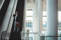 Longe de homem de negócios com pasta falando ao telefone na escada rolante no escritório — Fotografia de Stock