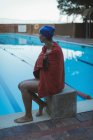 Вид збоку молодої жінки плавець, загорнутий в рушник, що сидить біля басейну — стокове фото