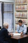 Vista trasera de un joven médico asiático y un paciente mayor que interactúan entre sí en la clínica - foto de stock