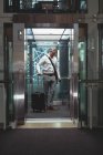 Front view of a businessman with travel suitcase waiting in the elevator in office — Stock Photo