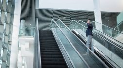 Low view of businessman talking on the mobile phone on escalator in office — Stock Photo