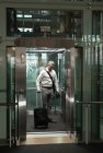 Front view of a businessman with travel suitcase looking at the command in the elevator in office — Stock Photo