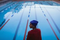 Вид спереду молодої жінки плавець, загорнутий в рушник, що стоїть біля басейну — стокове фото