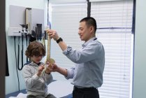 Vue latérale du jeune médecin masculin asiatique montrant le modèle de colonne vertébrale au patient garçon caucasien — Photo de stock