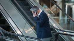 Вид збоку бізнесмена, який розмовляє на мобільному телефоні на ескалаторі в офісі — стокове фото