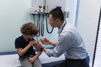 Vista lateral de joven asiático médico inyectando jeringa a niño caucásico paciente en clínica - foto de stock