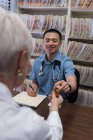 Vue de face du jeune médecin asiatique et du patient âgé interagissant les uns avec les autres à la clinique — Photo de stock