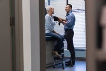 Visão lateral do médico masculino verificando a pressão arterial do medidor de pressão arterial do paciente sênior na clínica — Fotografia de Stock