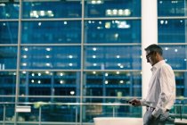 Seitenansicht eines Geschäftsmannes, der nachts sein Handy gegen ein Bürogebäude richtet — Stockfoto