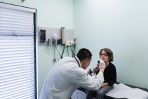 Rückansicht junger asiatischer Arzt untersucht kaukasischen Patienten mit Werkzeug in einer Klinik — Stockfoto