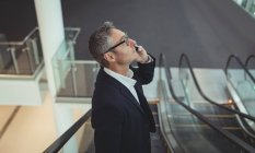 Vista laterale dell'uomo d'affari che parla al cellulare sulla scala mobile in ufficio — Foto stock