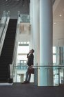 Side view of businessman with briefcase talking on the phone near the escalator in office — Stock Photo