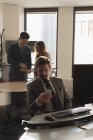 Vista lateral de hombre de negocios sentado utilizando el teléfono móvil en la oficina moderna con compañeros de trabajo discutiendo sobre tableta digital int él fondo - foto de stock