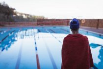 Vista trasera de una joven nadadora envuelta en una toalla cerca de la piscina - foto de stock