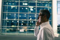 Seitenansicht eines Geschäftsmannes, der nachts vor einem Bürogebäude telefoniert — Stockfoto