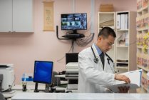 Вид сбоку на молодого врача мужского пола с отчетом о состоянии пациента на клинике — стоковое фото