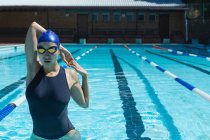 Vista frontale del giovane nuotatore femminile con occhiali da bagno che si estende in piscina in una giornata di sole — Foto stock