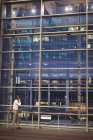 Visão traseira do empresário falando no telefone celular enquanto olha para um edifício através de janelas à noite — Fotografia de Stock