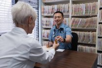 Vista frontale del giovane medico maschio asiatico e paziente anziano che interagisce tra loro in clinica — Foto stock