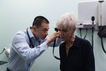 Vista frontal de un joven médico asiático examinando a un paciente mayor en la clínica - foto de stock