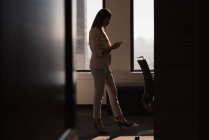 Vista lateral de empresária de pé usando telefone celular na sala de conferências no escritório — Fotografia de Stock