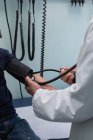 Vue latérale du jeune médecin masculin asiatique vérifiant la pression artérielle du patient garçon caucasien en clinique — Photo de stock