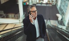 Frontansicht eines Geschäftsmannes, der auf der Rolltreppe im Büro mit dem Handy spricht — Stockfoto