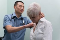 Primer plano del joven médico asiático examinando a un paciente mayor en la clínica - foto de stock