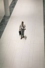 Vista elevata dell'uomo d'affari con la valigia da viaggio che guarda il suo cellulare mentre cammina nel corridoio — Foto stock