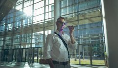Seitenansicht eines Geschäftsmannes, der im Büro gegen grelles Sonnenlicht dem Lautsprecher seines Smartphones lauscht — Stockfoto
