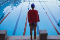 Вид сзади на молодую пловчиху, завернутую в полотенце, стоящую у бассейна — стоковое фото