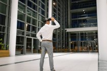 Vista trasera del hombre de negocios que experimenta auriculares VR fuera de la oficina por la noche - foto de stock