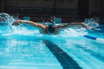 Frontansicht eines männlichen Schwimmers mit Schwimmbrille, der den Schmetterling im Schwimmbad schwimmt — Stockfoto
