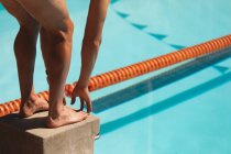 Low section of male swimmer standing on starting block in starting position at swimming pool in the sunshine — Stock Photo