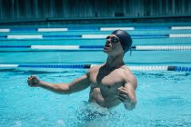 Збоку подання молодих кавказьких чоловіків плавець з обіймами, витягнув у перемозі святкувати у відкритому басейні на сонячний день — стокове фото