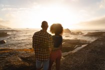Rückansicht eines afrikanisch-amerikanischen Paares, das in der Nähe des Meeres steht und relaxt. sie schauen auf den Horizont — Stockfoto
