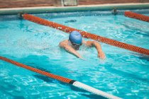 Vue latérale du jeune nageur masculin caucasien nageant coup de papillon dans la piscine extérieure au soleil — Photo de stock