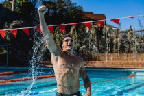 Вид спереду збудженого чоловічого плавця, який святкує свою перемогу і піднімає кулак у басейні — стокове фото