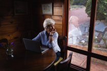 Vorderansicht einer nachdenklichen aktiven Seniorin, die mit einem Laptop sitzt und arbeitet, während sie zu Hause wegschaut — Stockfoto